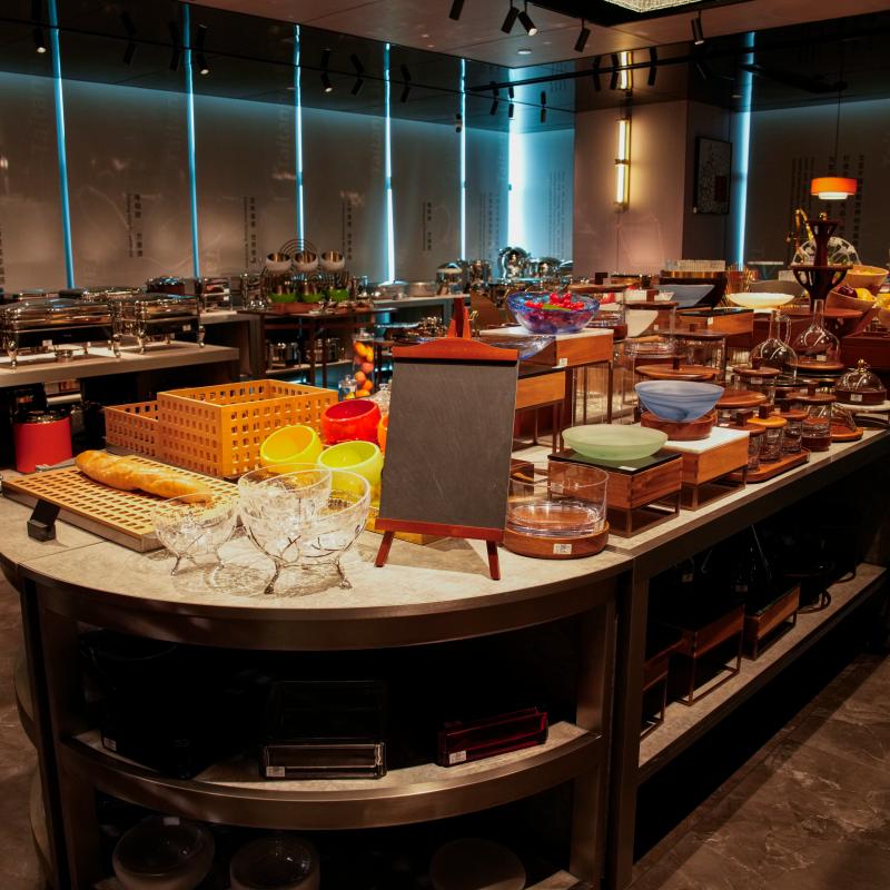 A wide-angle view of a beautifully arranged, curved wooden buffet station by Taitang Hospitality. It features organized bread displays, serving bowls, and a small blank chalkboard menu.JPG