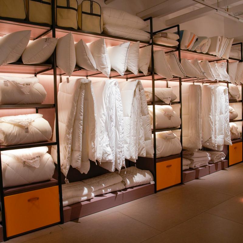 Taitang hotel linen supplier showroom displaying premium white hotel bedding sets, duvets, and pillows on warm backlit shelves.JPG