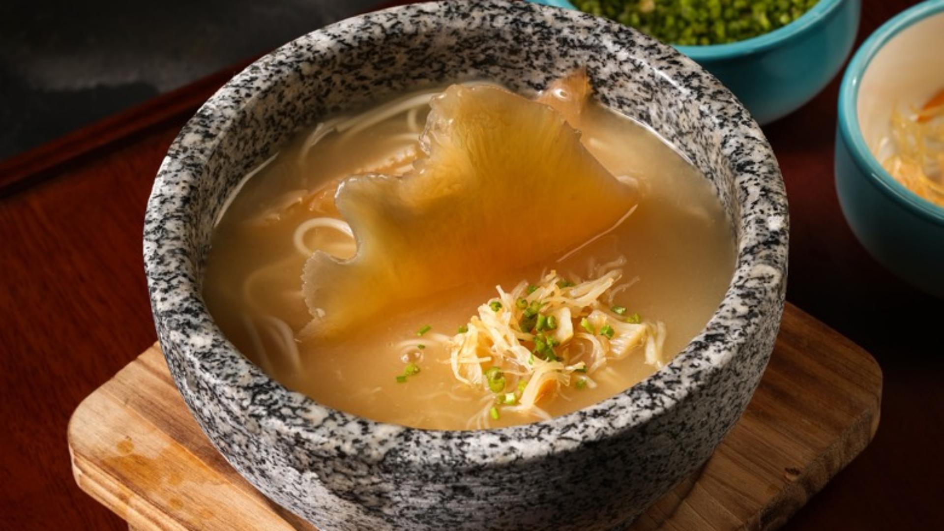 Gourmet Chinese braised soup served in a heat-retaining natural granite stone bowl on a wooden serving board.jpg