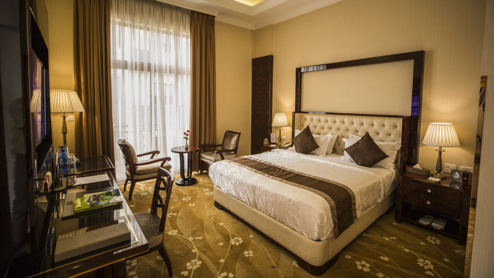 A well-appointed, luxurious interior view of a guest room at the Sapphire Addis Hotel, featuring a neatly made bed with white linens and dark brown accent pillows.jpg
