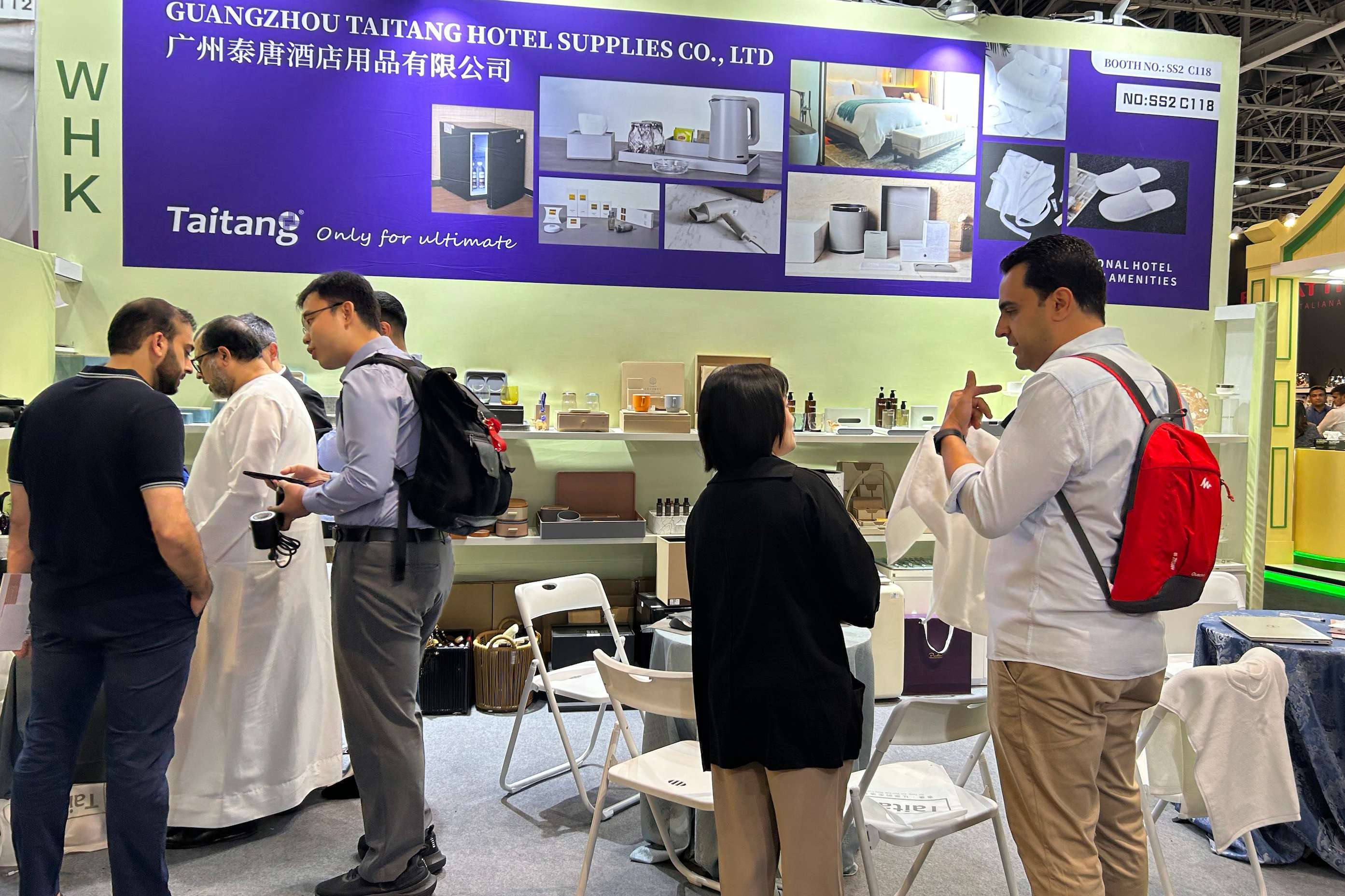TAITANG staff engaging with a diverse group of international buyers, showcasing professional guestroom amenities at a global hotel supplies expo.