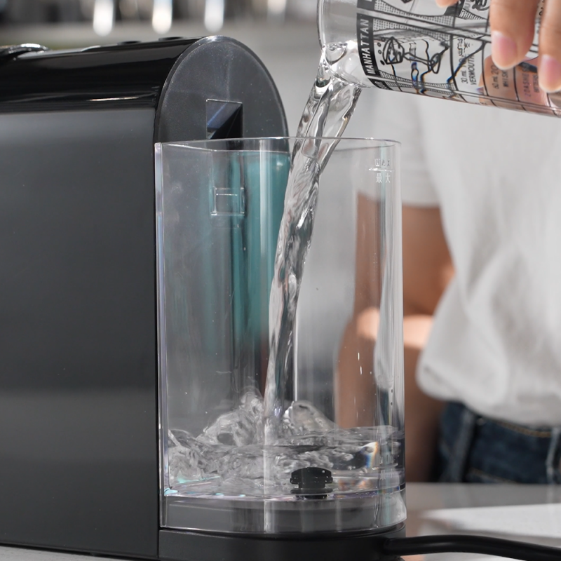 Pouring fresh water into the transparent removable water reservoir of a black Taitang hotel capsule coffee machine.png