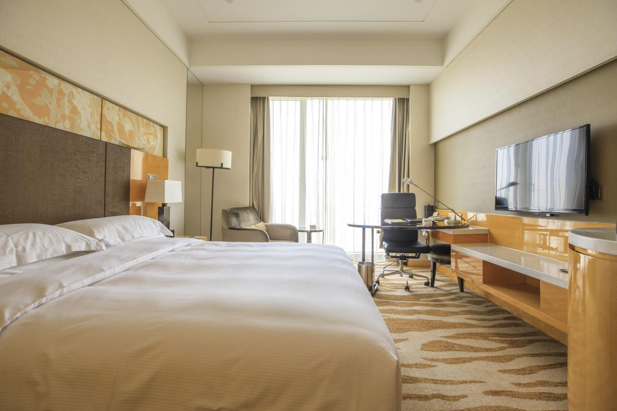 A high-end, modern hotel suite featuring a king-size bed with premium white linens, a wooden work desk, and a wall-mounted TV, showcasing the successful implementation of Taitang's furniture and supply solutions.