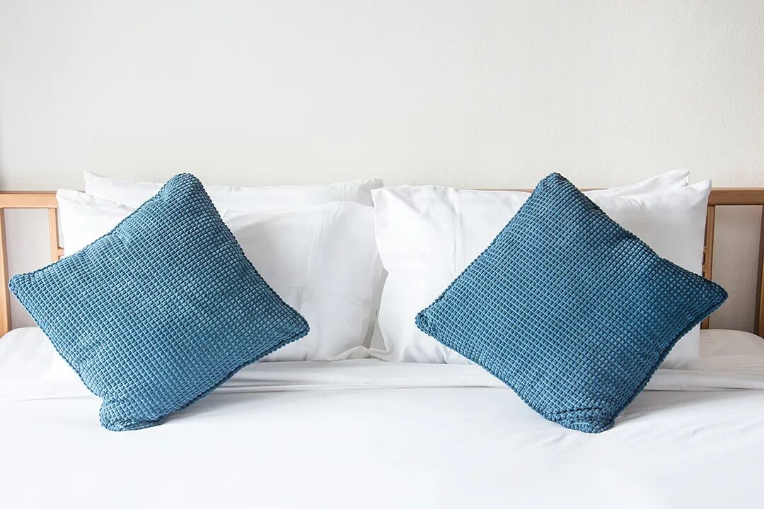 White hotel bedding accented with textured blue decorative pillows, demonstrating how TAITANG linens balance classic hygiene with modern aesthetic sophistication.
