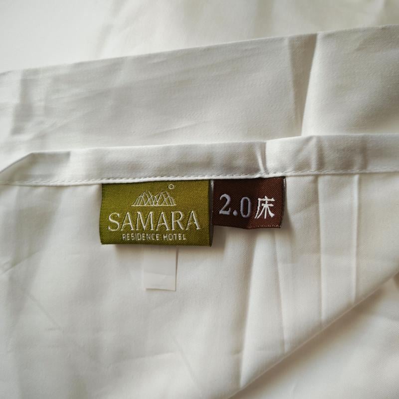 Close-up of luxury white hotel bed sheet featuring a custom sewn SAMARA RESIDENCE HOTEL woven brand label and bed size tag..jpg