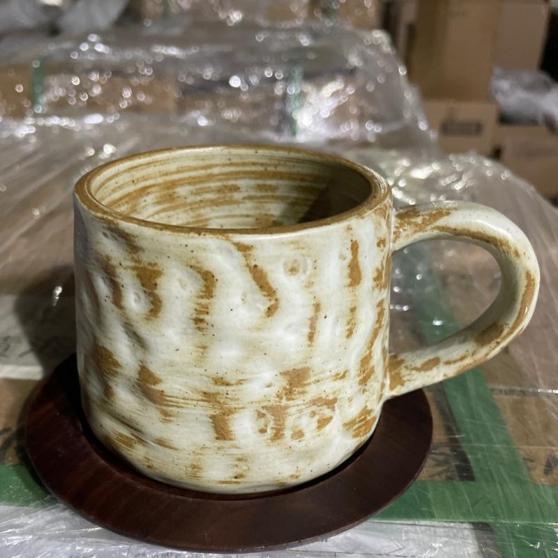 Textured beige-and-white glazed ceramic mug with ergonomic handle set on a dark hardwood saucer.JPG