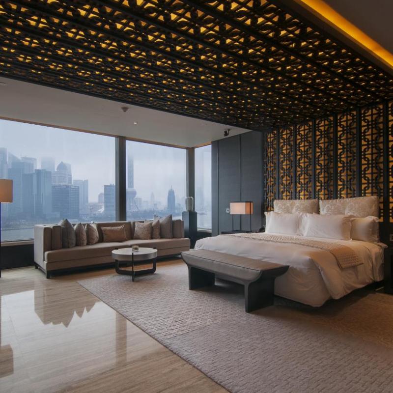 A penthouse hotel suite with high ceilings, a geometric light feature, and extensive floor-to-ceiling windows, highlighting how space and architecture contribute to the sense of luxury.jpg