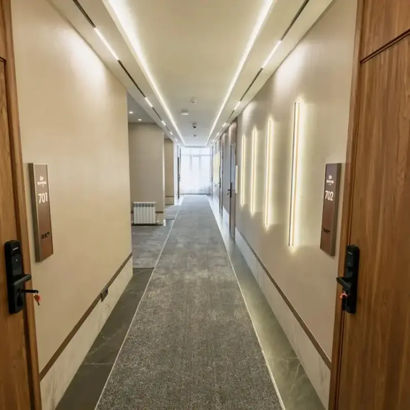 Well-lit hotel floor hallway with warm wall lighting, carpeted flooring, and smart electronic room doorplates.webp