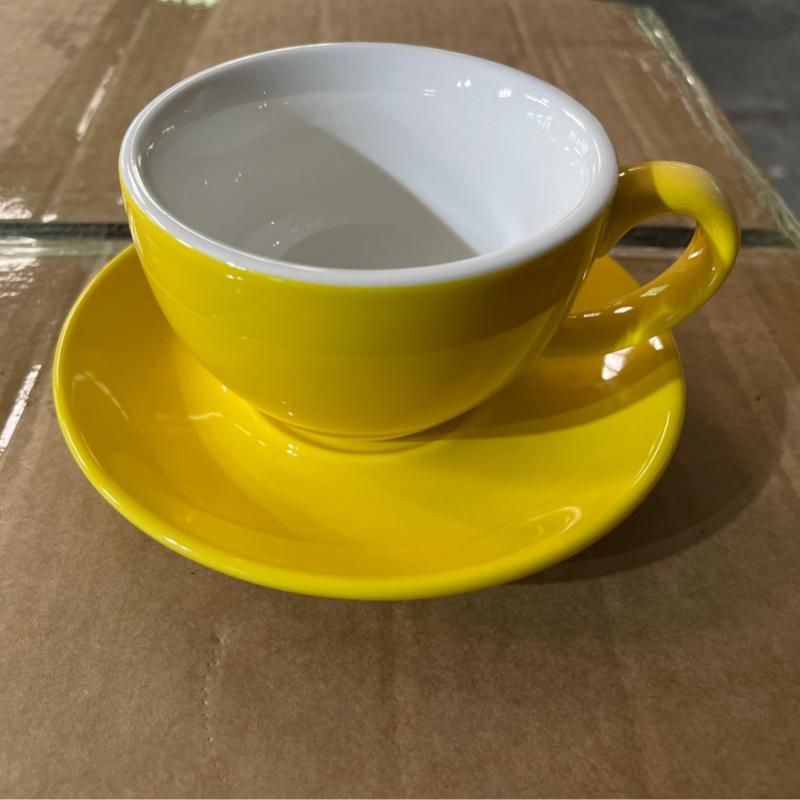 Bright yellow glazed hotel ceramic cappuccino cup and saucer set resting on a packaging box during pre-shipment quality checks.JPG
