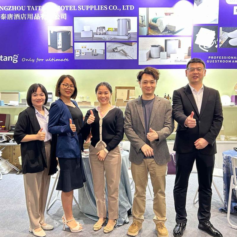 Five Taitang representatives standing together and giving thumbs-up gestures in front of their commercial hotel products display in Dubai.jpg