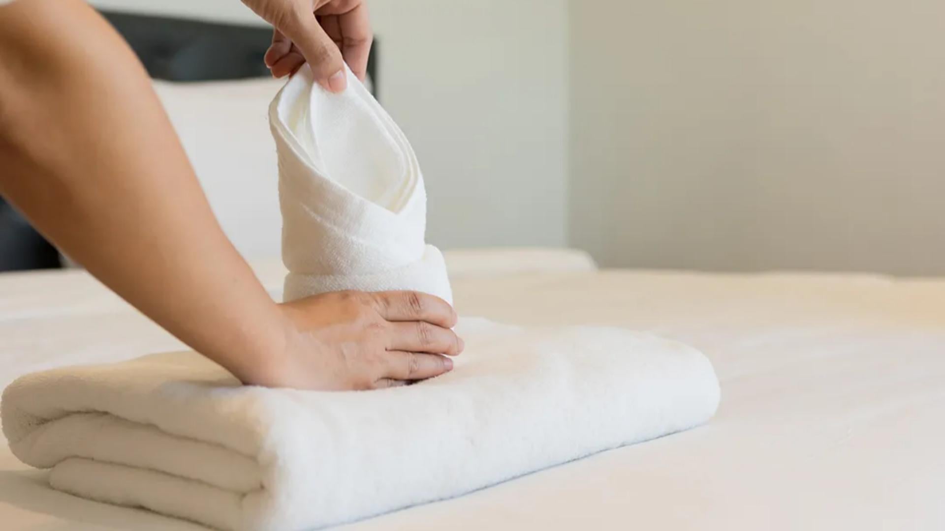Housekeeping staff folding a premium white Taitang hotel bath towel on a guest room bed, emphasizing neatness and brand consistency..jpg