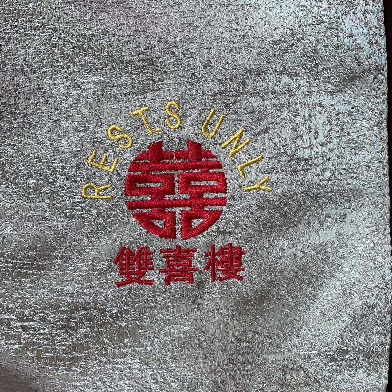 Close-up of silver textured banquet tablecloth featuring custom embroidered gold REST. SUNLY text and red Double Happiness logo.JPG