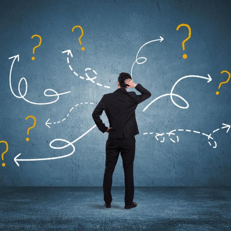 Businessman facing a wall with question marks and directional arrows, depicting complex planning and decision-making for a hotel opening countdown.jpg