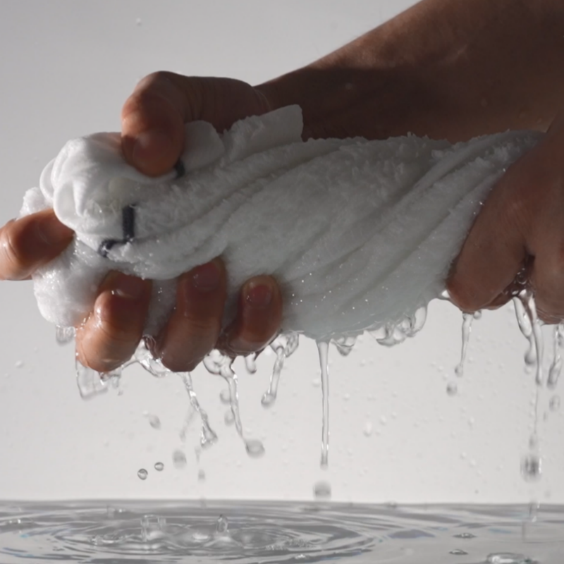 Hands wringing water from a commercial white cotton hotel towel demonstrating rapid absorbency and fiber durability.png
