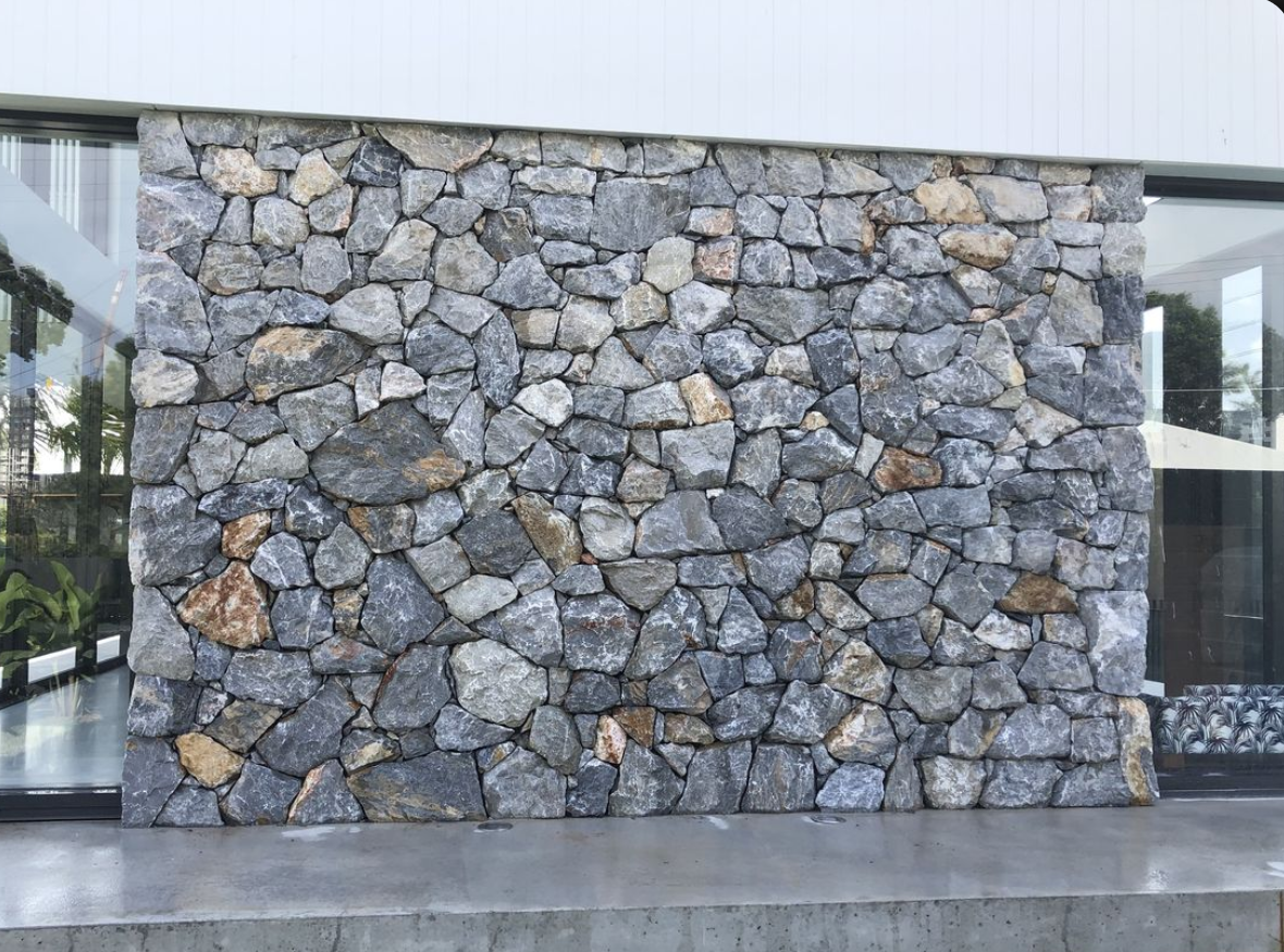 Mixed grey loose stone installed as exterior wall cladding