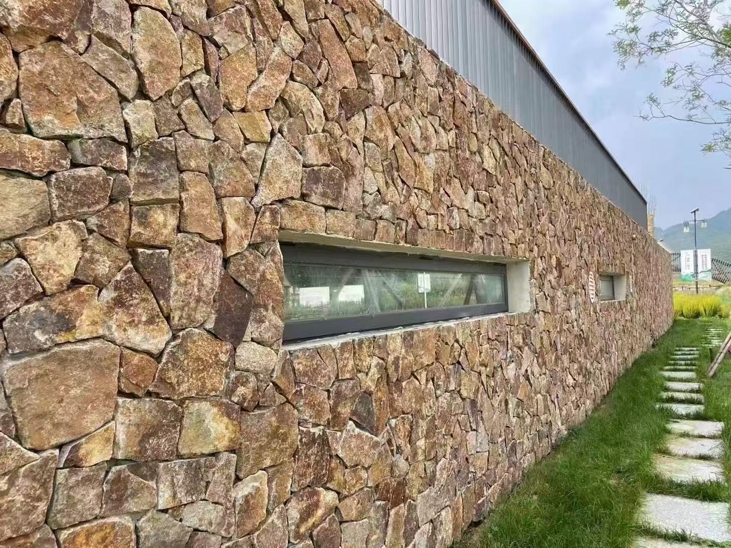 Warm irregular natural stone cladding on a long exterior facade