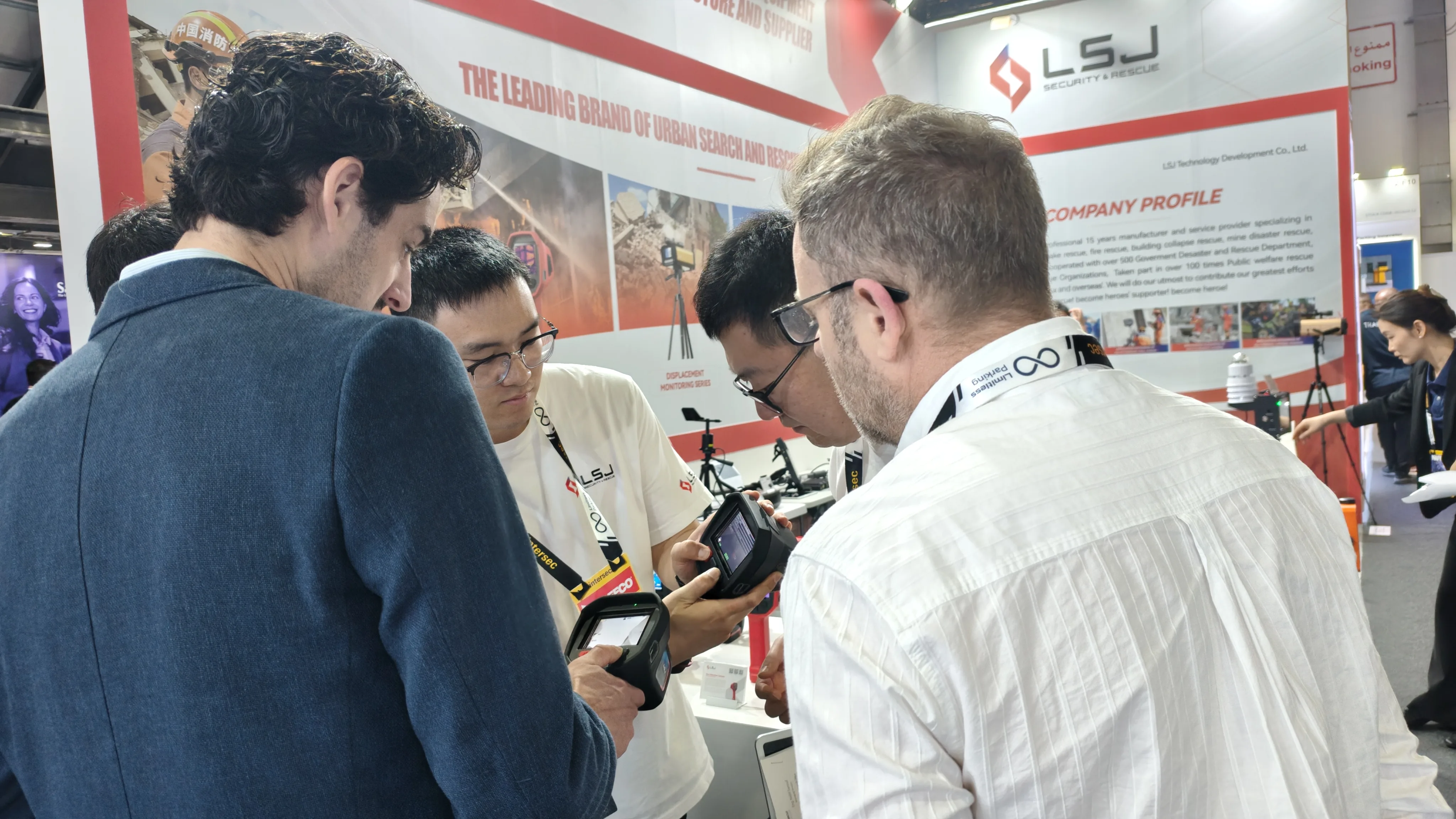 IMG-09 | LSJ Handheld Detection Equipment Close-up Close-up of LSJ staff reviewing a handheld detection device with two international clients at the busy INTERSEC 2026 Dubai booth.