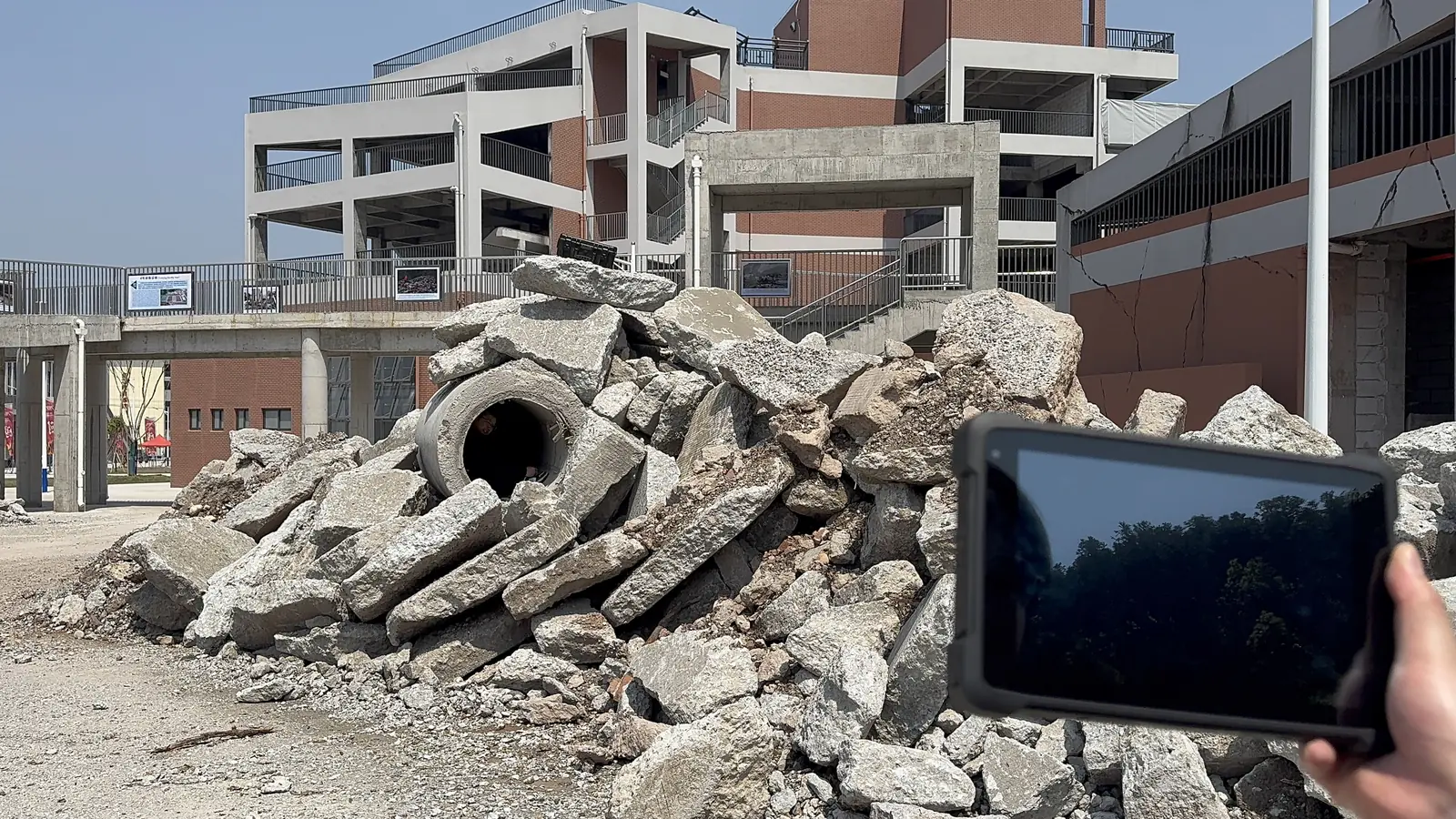Rescuer holding the LSJ-M rugged Android handheld terminal and reading survivor location data in front of a concrete rubble search pile
