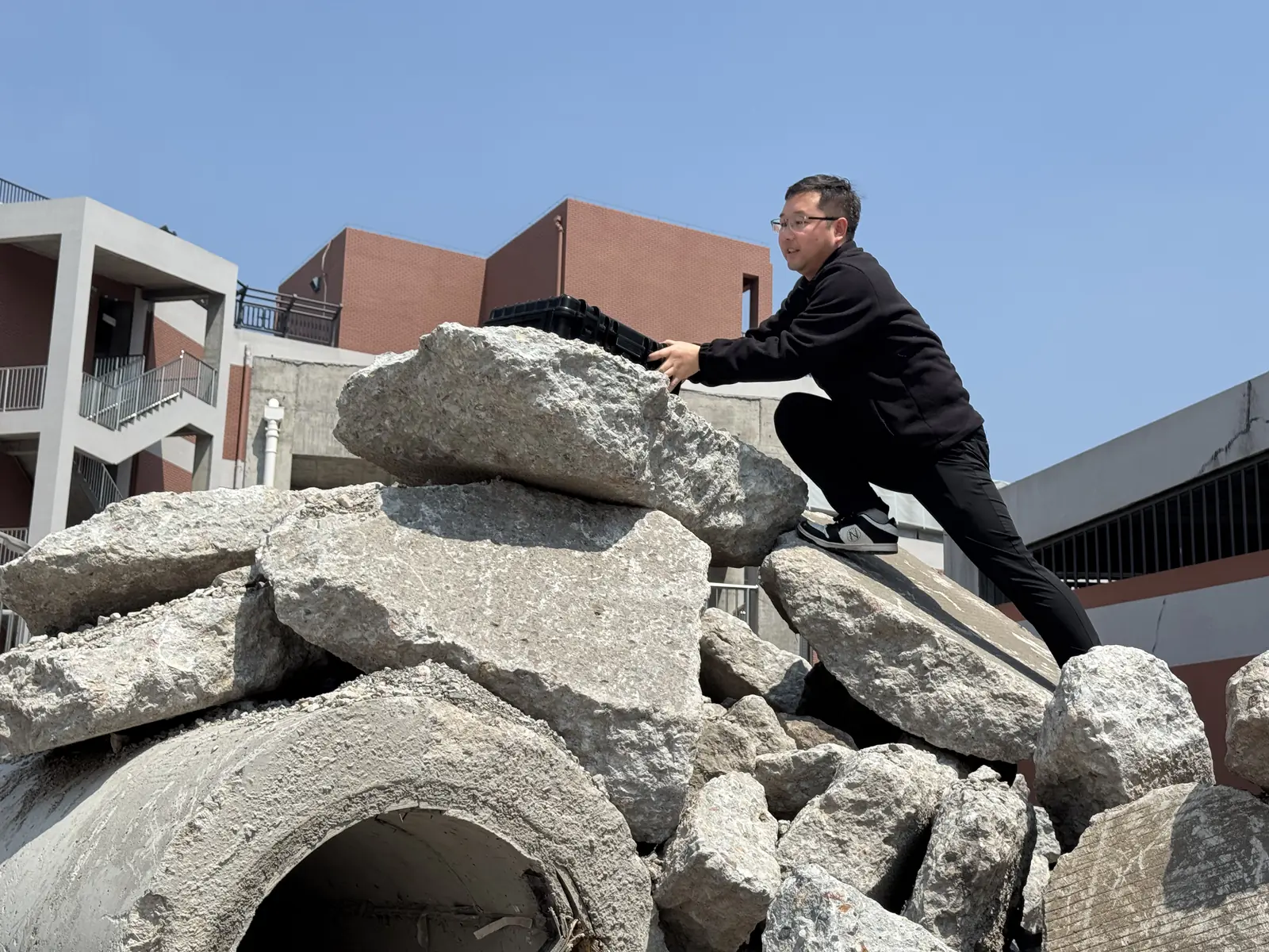 Rescue operator positioning the black LSJ-M radar host on top of a concrete rubble pile before starting a survivor search at a training site