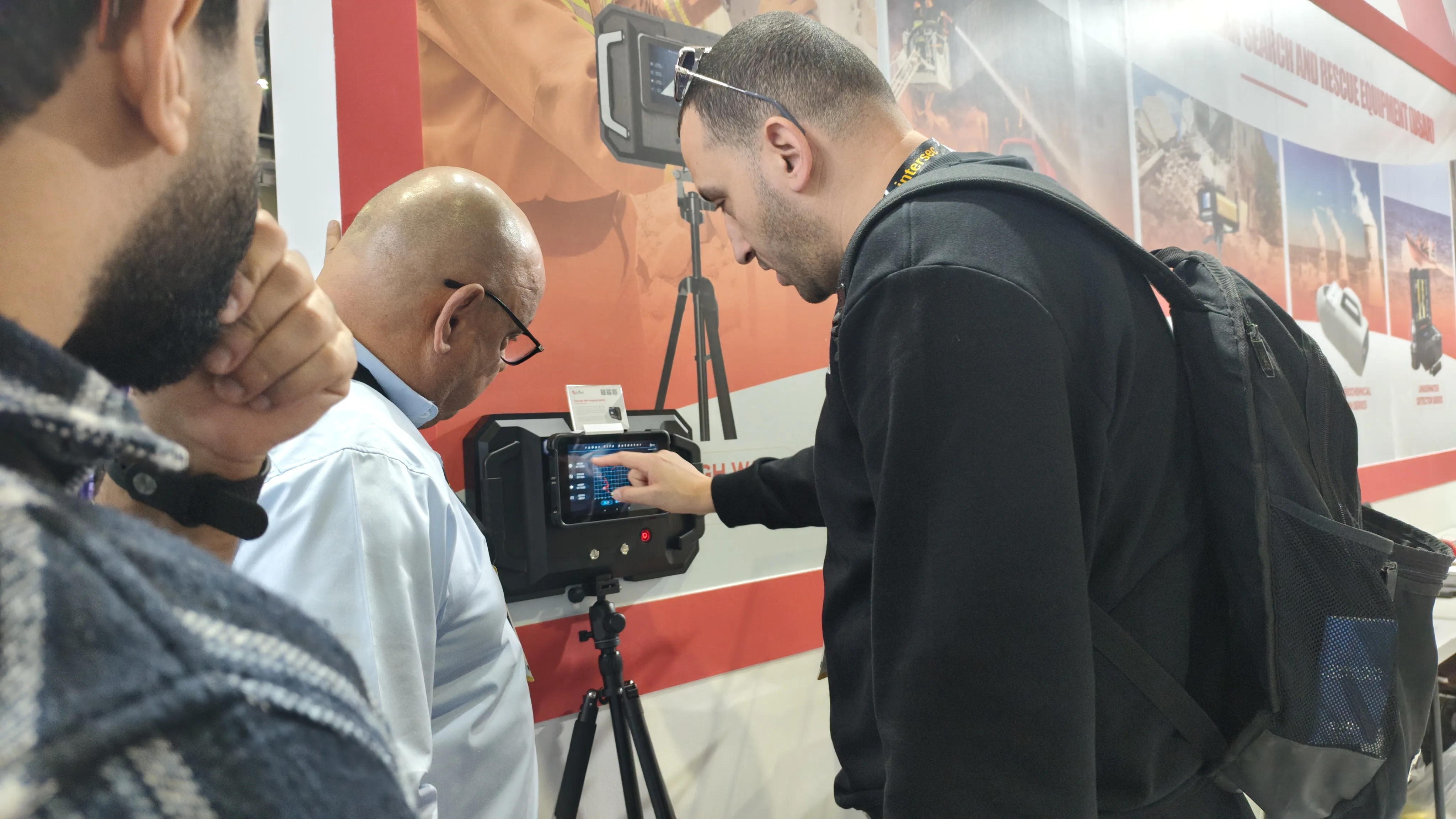 IMG-06 | Visitors Exploring LSJ Detection Solutions A show visitor closely inspecting an LSJ detection device mounted on a tripod while a product specialist explains the solution at INTERSEC 2026.